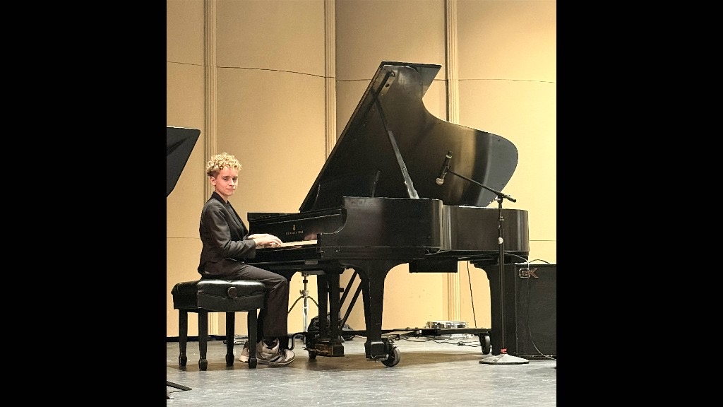 Leland at a Steinway grand piano on stage, smiling at the camera
